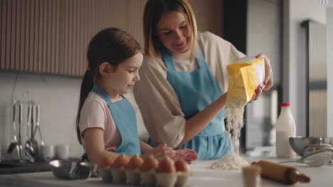 Mutter-Und-Kind-Kochen-Zu-Hause,-Frau-Schüttet-Mehl-Auf-Den-Tisch,-Kleines-Mädchen-Hilft-Beim-Kochen